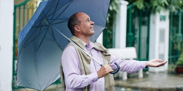 Elderly Man Smiling Under Umbrella at Assisted Living Facility