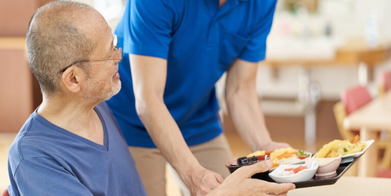 Nursing Staff Serving a Meal Tray to an Elderly Resident at a Memory Care Facility